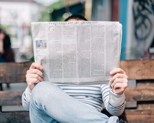 man-sitting-on-bench-reading-newspaper
